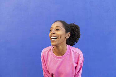 Fröhliche Frau mit Afrofrisur vor blauem Hintergrund - LMCF00201