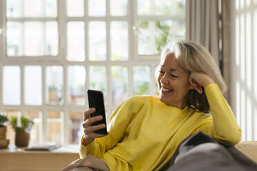 Glückliche reife Frau benutzt Handy auf Sofa zu Hause - EBSF02777