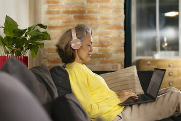 Freiberufler mit kabellosen Kopfhörern bei der Arbeit am Laptop zu Hause - EBSF02790