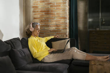Älterer Freiberufler mit drahtlosen Kopfhörern, der zu Hause am Laptop arbeitet - EBSF02791