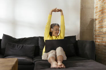 Smiling freelancer stretching arms sitting on sofa at home - EBSF02794