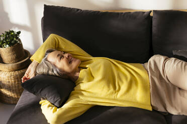 Smiling mature woman relaxing on sofa in living room - EBSF02800