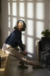 Smiling woman sitting by wall at home - EBSF02825