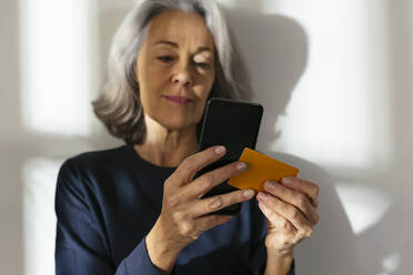 Reife Frau, die zu Hause mit Kreditkarte auf dem Smartphone bezahlt - EBSF02830