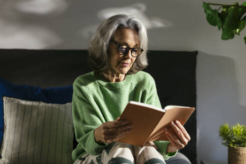 Lächelnde Frau liest ein Buch auf dem Bett zu Hause - EBSF02838