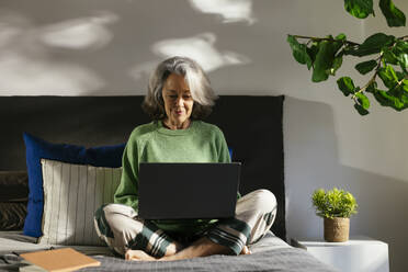 Smiling woman using laptop on bed at home - EBSF02840