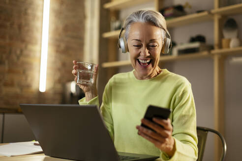 Glückliche Frau mit einem Glas Wasser und einem Smartphone zu Hause - EBSF02886