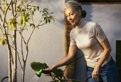 Lächelnde Frau mit grauem Haar, die Pflanzen gießt - EBSF02896