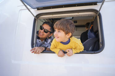 Father and son looking through window of camper van - FBAF02088