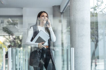 Businesswoman talking on smart phone seen through glass - JSRF02411