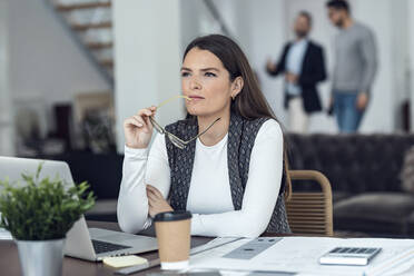 Thoughtful businesswoman with eyeglasses sitting at desk - JSRF02415