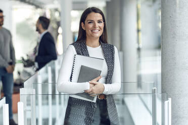 Happy businesswoman standing with diary at office - JSRF02418