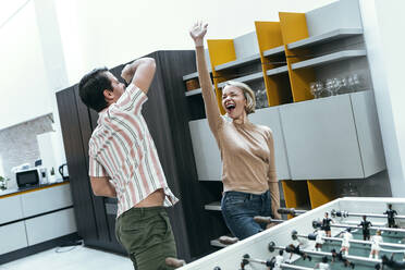 Cheerful businesswoman and businessman playing foosball at office - JSRF02441