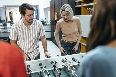 Fröhliche Kollegen spielen zusammen im Büro Tischfußball - JSRF02447