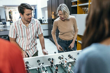 Happy colleagues playing foosball together at office - JSRF02447