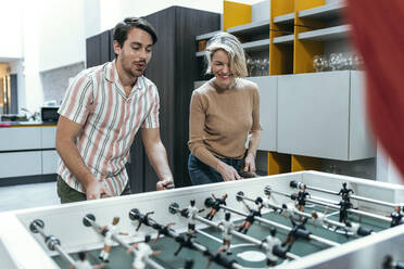 Cheerful businesswoman and businessman playing foosball at office - JSRF02450