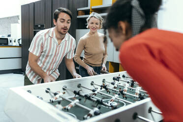 Happy coworkers playing foosball at office - JSRF02451