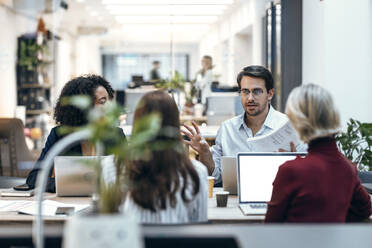 Businessman discussing with colleagues at desk - JSRF02454