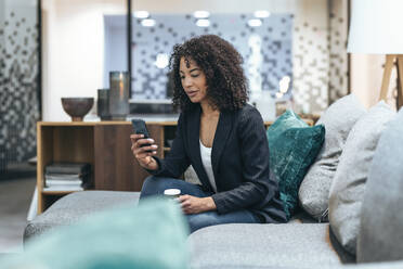 Geschäftsfrau benutzt Smartphone auf Sofa am Arbeitsplatz - JSRF02461
