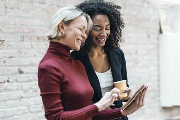 Glückliche Geschäftsfrauen, die im Büro über einen Tablet-PC diskutieren - JSRF02464