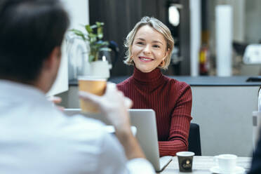 Lächelnde Geschäftsfrau im Gespräch mit einem Kollegen am Schreibtisch - JSRF02468