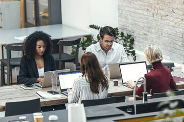 Businessman and businesswomen working on laptop at desk - JSRF02472