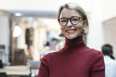 Happy businesswoman wearing eyeglasses at office - JSRF02475
