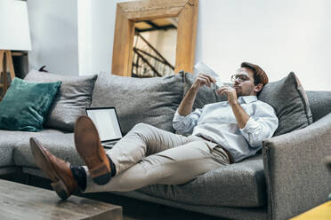 Businessman with paper airplane sitting on sofa at office - JSRF02477