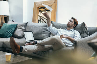 Businessman playing with paper airplane on sofa at office - JSRF02478