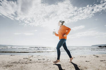 Frau joggt am Strand an einem sonnigen Tag - AAZF00086