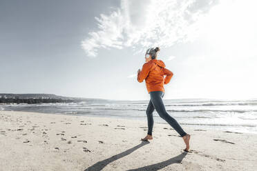 Mature woman jogging on shore at beach - AAZF00087