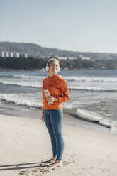 Lächelnde reife Frau mit Wasserflasche am Strand stehend - AAZF00093