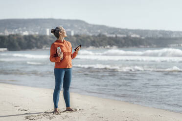 Mature woman standing on sand at beach - AAZF00097