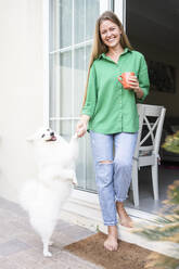 Glückliche Frau mit süßem Hund vor der Tür stehend - SVKF01280