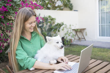 Freiberufler mit Hund benutzt Laptop im Garten - SVKF01286