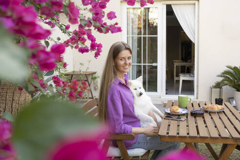 Smiling woman sitting with cute dog in garden - SVKF01307