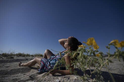 Woman with head in hand lying on sand at sunny day - AXHF00285