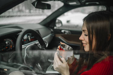 Smiling woman having coffee sitting in car - ANAF01044