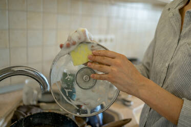 Woman washing lid with scouring pad in kitchen at home - ANAF01046