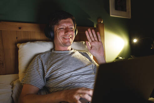 Smiling man waving on video call in bedroom at home - TYF00752
