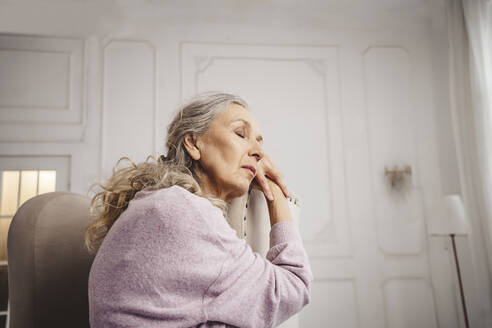 Senior woman with eyes closed sitting on chair at home - MDOF00641
