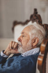 Nachdenklicher älterer Mann sitzt zu Hause auf einem Stuhl - MDOF00652