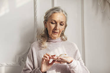 Smiling senior woman with butterfly on hand at home - MDOF00653