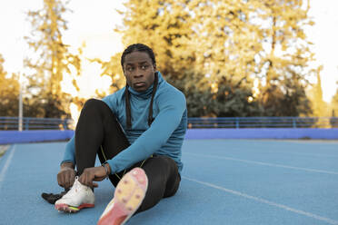 Thoughtful athlete tying shoelace sitting on sports track - JCCMF09485