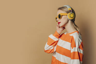 Frau mit drahtlosen Kopfhörern vor braunem Hintergrund - VSNF00535