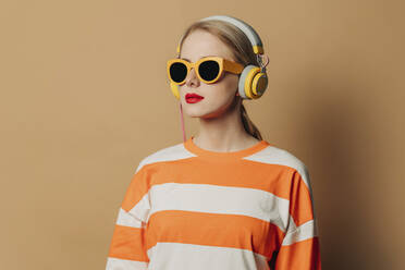 Frau mit Kopfhörern und Sonnenbrille vor einem braunen Hintergrund - VSNF00536