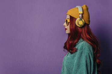 Rothaarige Frau hört Musik über Kopfhörer vor lila Hintergrund - VSNF00551