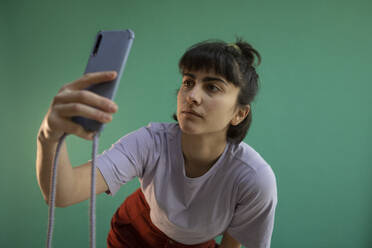 Junge Frau nimmt Selfie durch Smartphone gegen grünen Hintergrund - AXHF00287