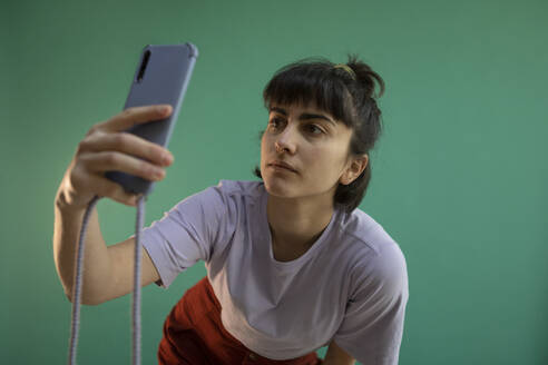 Young woman taking selfie through smart phone against green background - AXHF00287
