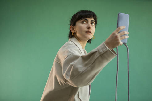 Woman photographing through smart phone against green background - AXHF00292